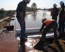 The wet curing process begins with covering the surface of the concrete with a 1/8” to 1/4” layer of water. Here the contractors are starting to roll out McTech Group’s UltraCure NCF™ curing blanket. This curing method is designed to provide thorough hydration and even curing. To learn more about UltraCure NCF™ go to http://www.mctechgroup.com/wc_train.html. UltraCure NCF™ is a registered trademark of McTech Group Inc. The concrete is colored with Davis Colors’ concrete color. www.daviscolors.com.